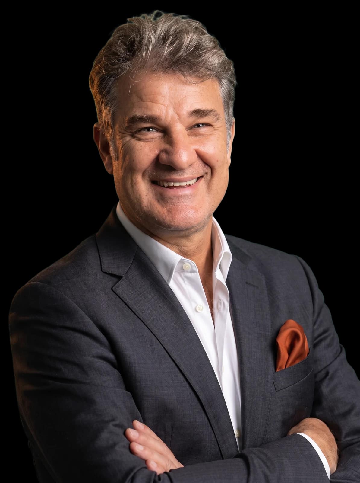 Daniel Santos Cori smiling with arms folded in a charcoal suit